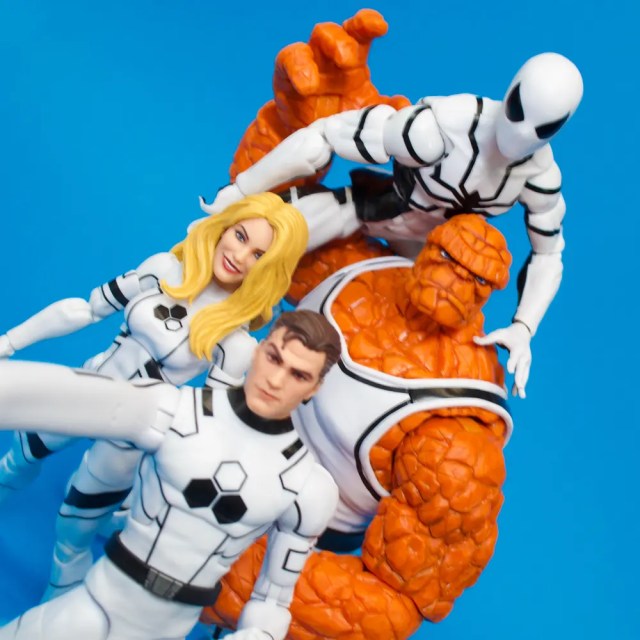 A group of four action figures from a superhero team, featuring characters in white and orange costumes posing together against a blue background.