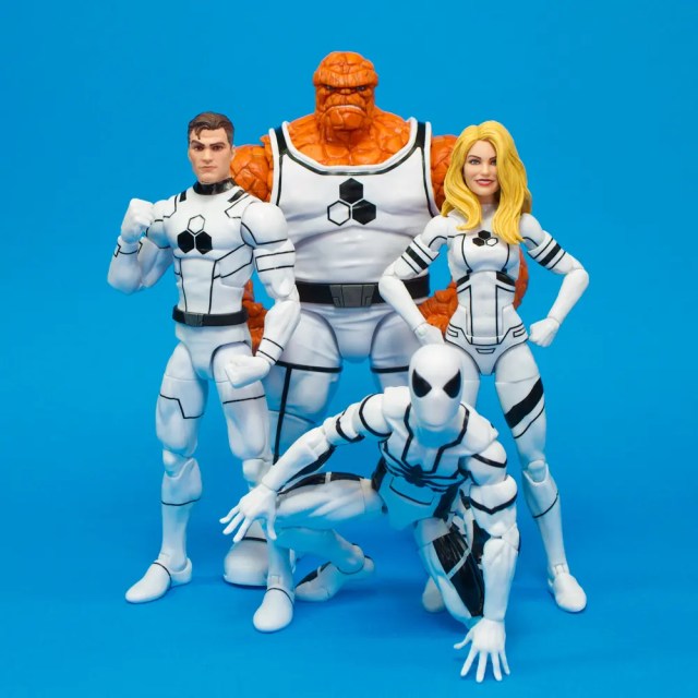 A group of four action figures from a superhero team, featuring characters in white and black suits against a blue background. The characters include a muscular orange figure, a man with a strong pose, a woman with long blonde hair, and a crouching figure in a white and black suit.