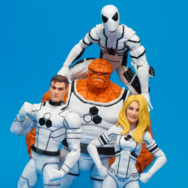 A group of four action figures in matching white and black costumes, featuring a muscular male figure, a female figure with long blonde hair, a rocky orange figure, and a figure dressed in a white costume with a black mask positioned on top.