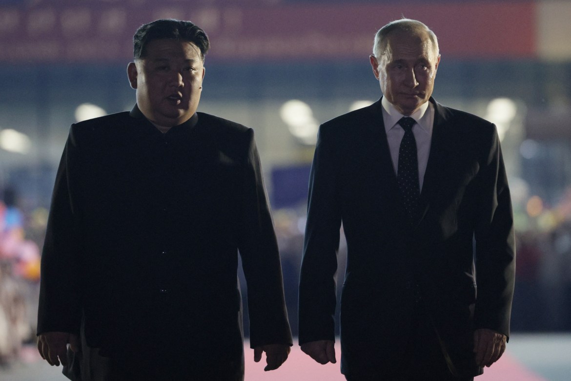 A somewhat dark and blurry photo taken at a distance shows Kim Jong Un, left, and Vladimir Putin, right, both in dark suits and walking side by side.