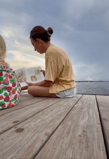Mom reading read aloud chapter book to toddler sitting on dock in Charleston, SC.