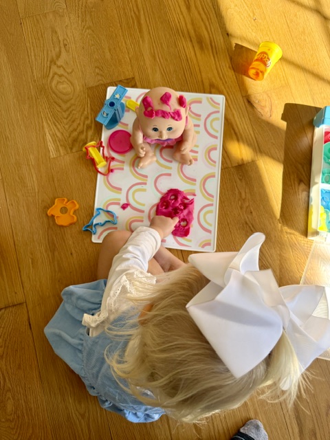 Toddler playing with play dough and baby doll during independent playtime. 
