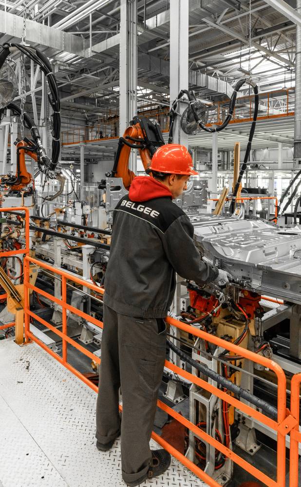 Photo of automobile production line. Welding car body. Modern car assembly plant. Auto industry. Male worker in an orange protective helmet