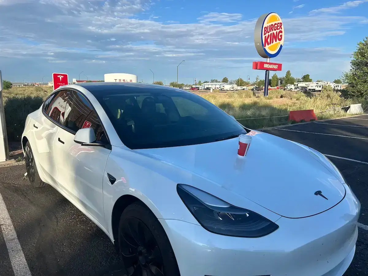 Tesla charging at a supercharger with a coffee on the hood of the car