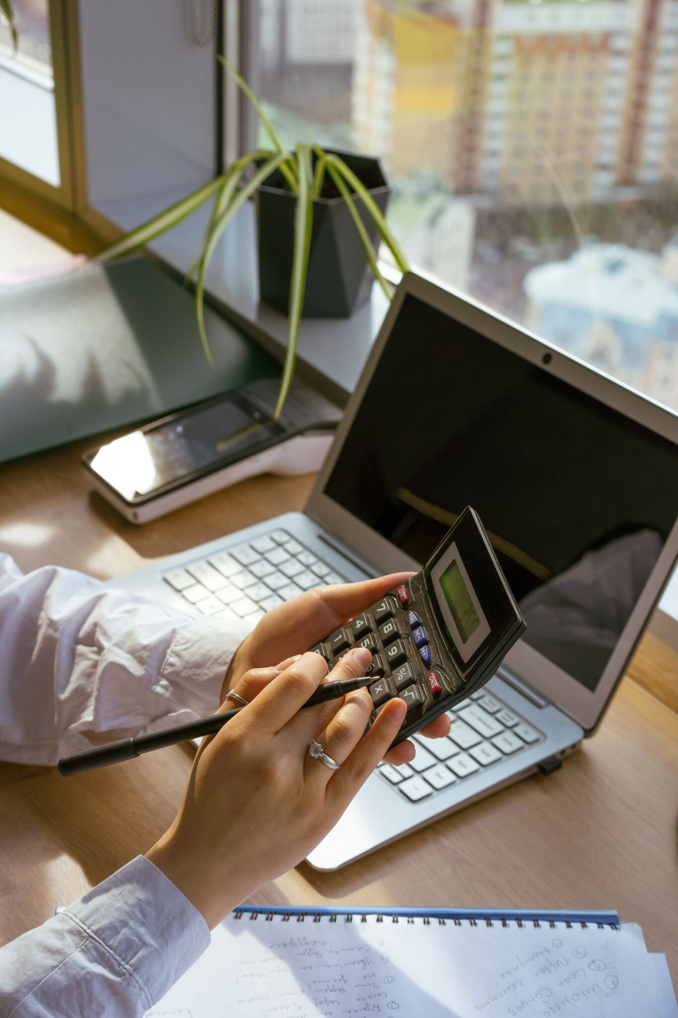 Person using a calculator and laptop to compare employee scheduling software vs spreadsheet costs