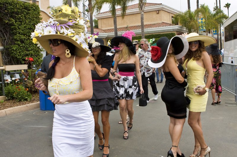 Group of women wearing various stylish hats and dresses at an outdoor event.