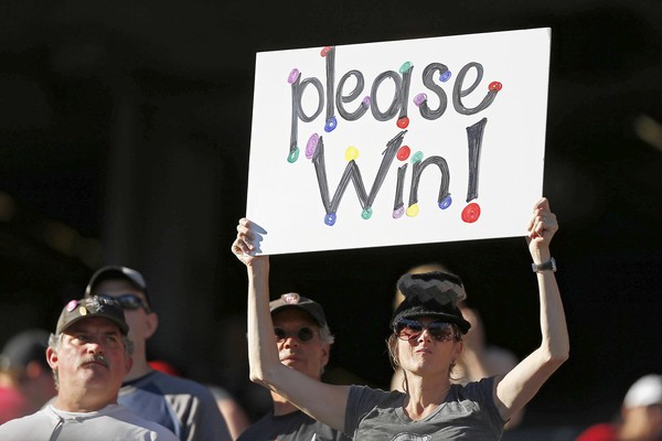 A fan holding a colorful sign that says 'please win' during a sporting event.