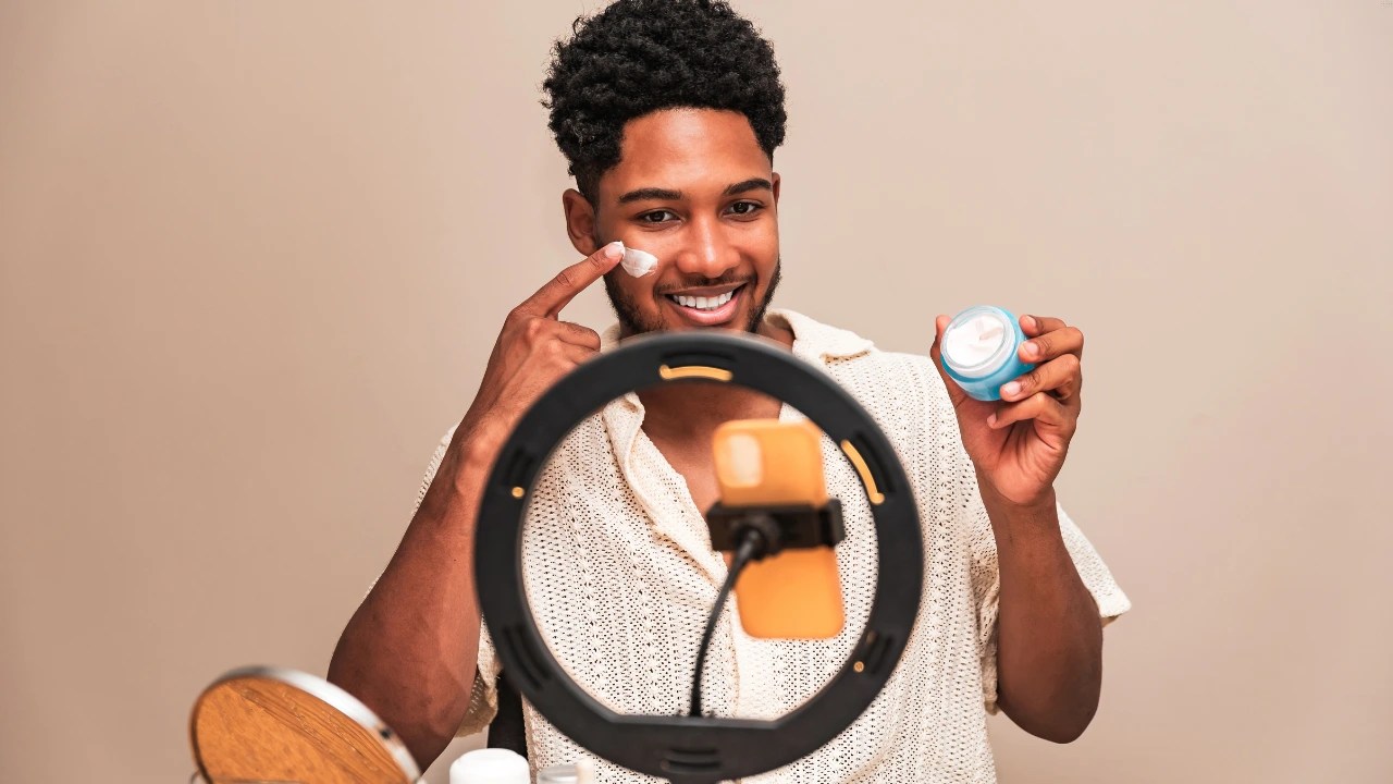 A male influencer demonstrating a beauty product to his audience using a smartphone mounted on a ring light