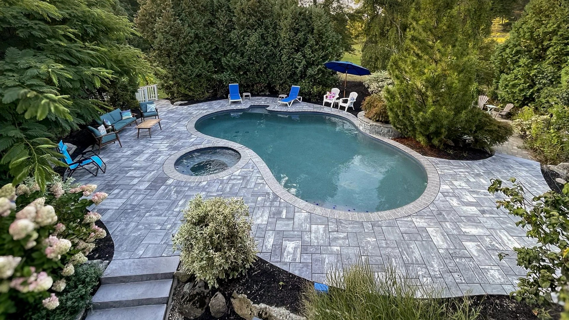 Freeform gunite pool design in Connecticut with spa, paver patio, and landscaped backyard