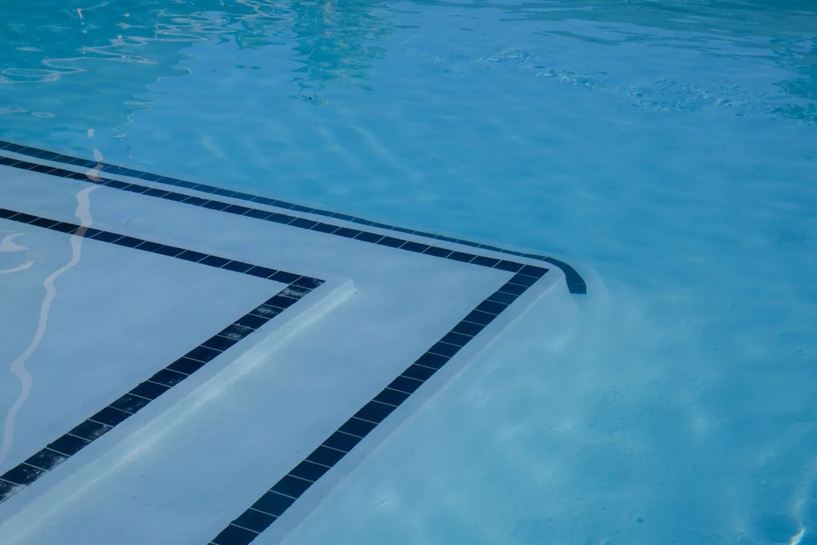 Submerged pool steps with dark tile trim in clear blue water