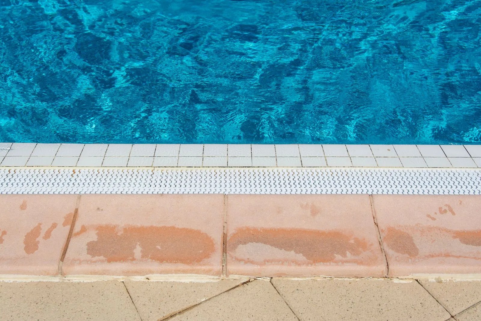 Pool waterline where the water meets white tile and stone coping