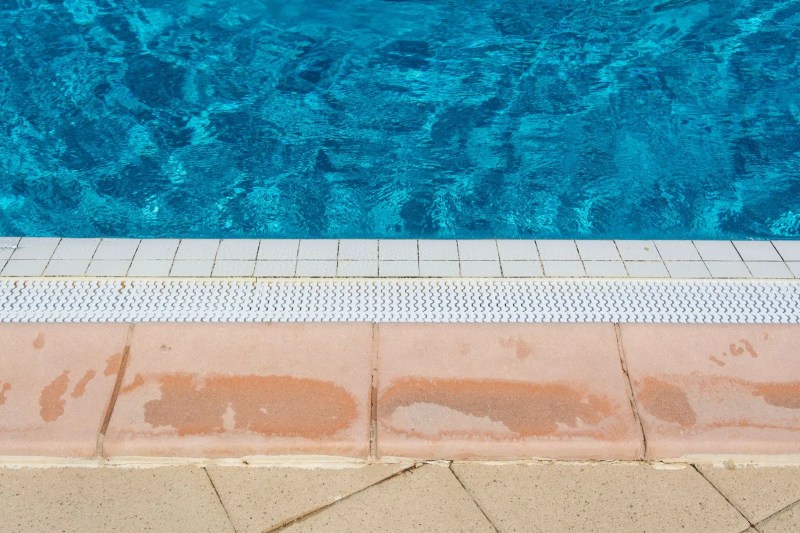 Pool waterline where the water meets white tile and stone coping