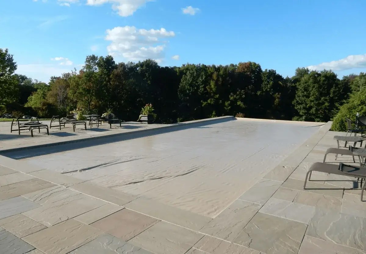 Tan automatic cover closed over a pool with a bluestone deck