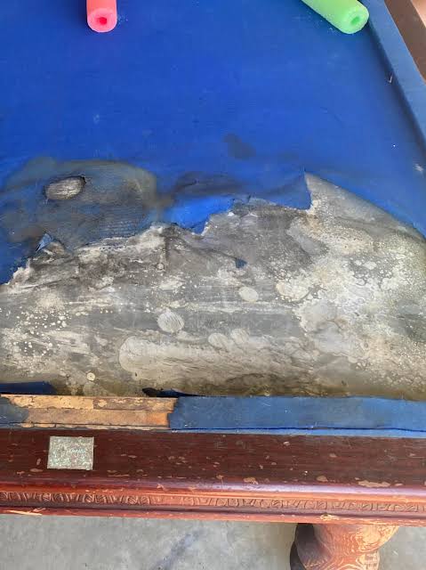 Damaged pool table slate exposed beneath torn blue cloth before professional repair
