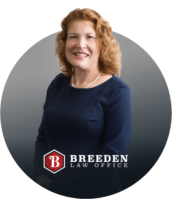 A woman with curly red hair, wearing a navy blue dress and pearl necklace, smiles in front of a gray background. The image features the Breeden Law Office logo at the bottom.