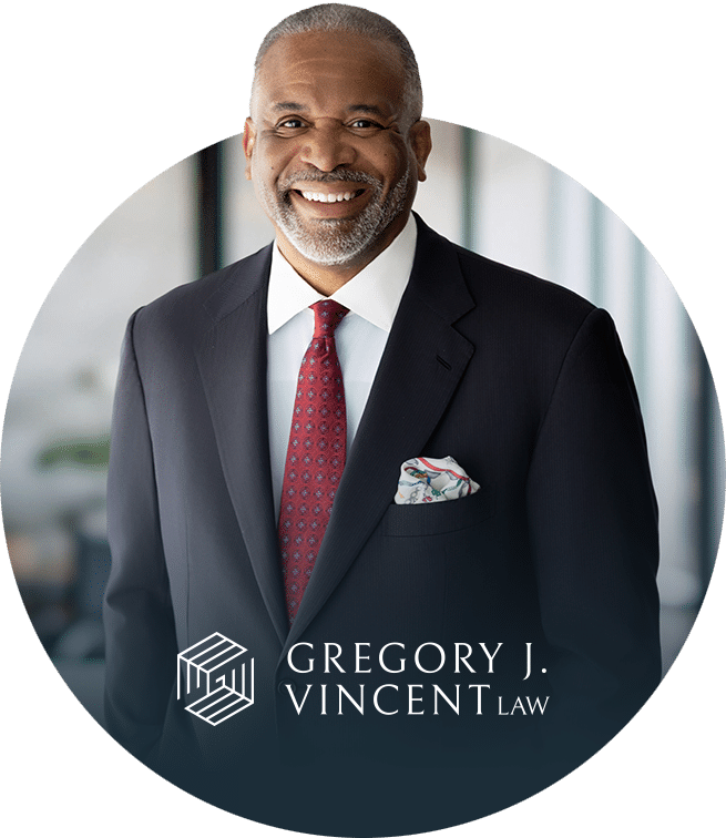 Smiling man in a dark suit, white shirt, and red tie stands indoors. A patterned pocket square is visible, and “Gregory J. Vincent Law” logo appears at the bottom of the image.