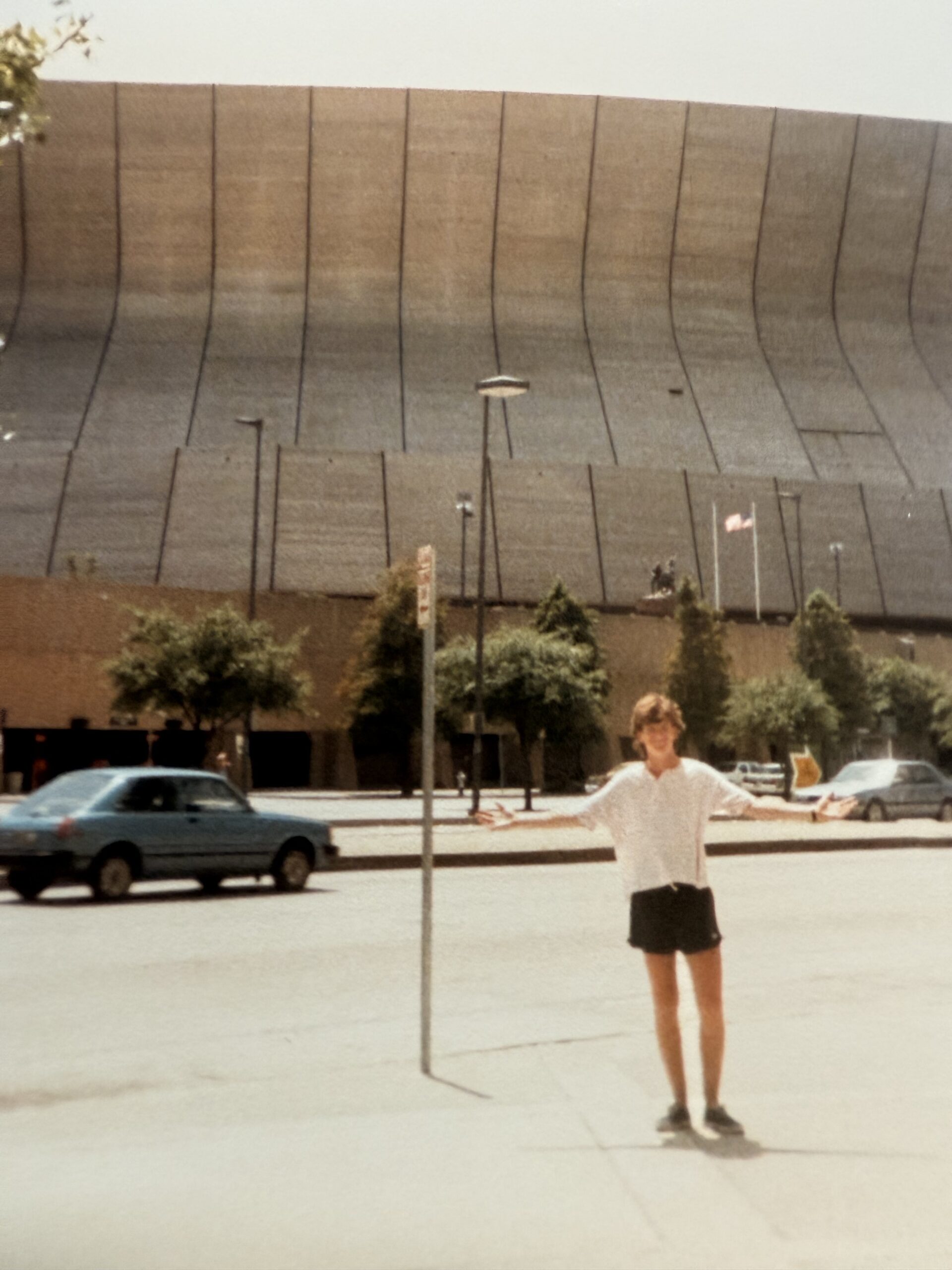 Young man stands outside the Superdome in New Orleans arms outstretched.