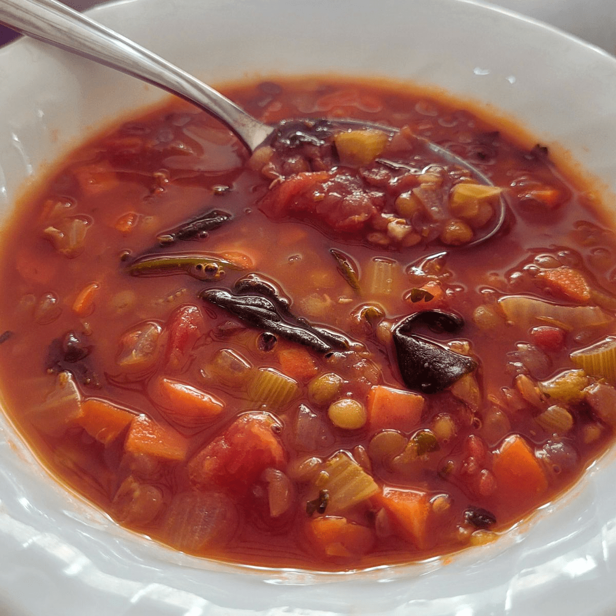 Easy lentil and vegetable soup sits in a white bowl with a silver spoon.
