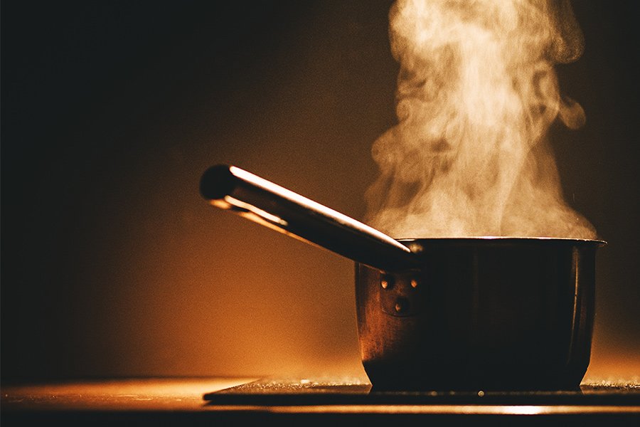 Panela com cabo com l&iacute;quido fervente e vapor sobre fog&atilde;o de indu&ccedil;&atilde;o em fundo escuro
