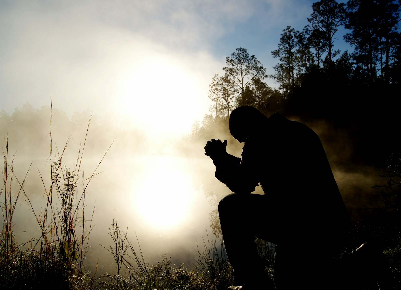 Silhouette of a man kneeling in prayer at dusk
