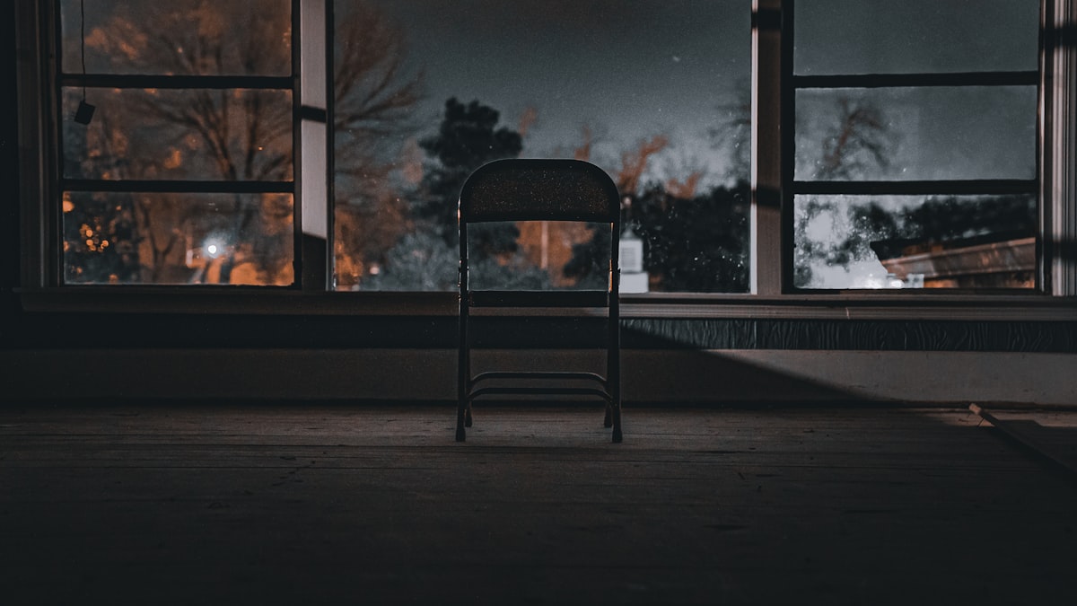 A chair by a window at night where someone prays against delay