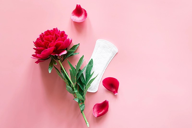 Maxibinde auf einem Tisch mit einer roten Blume, von der mehrere Blütenblätter entfernt wurden, um die Ovulationsblutung während deines Zyklus zu veranschaulichen