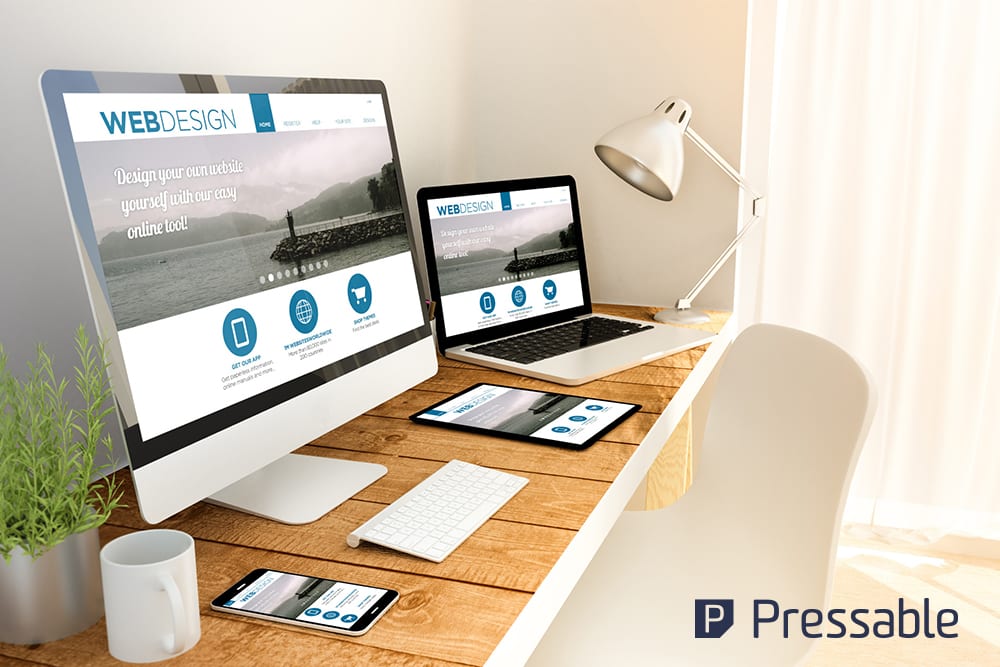 A desk displays multiple devices with website designs, surrounded by a lamp and plant.