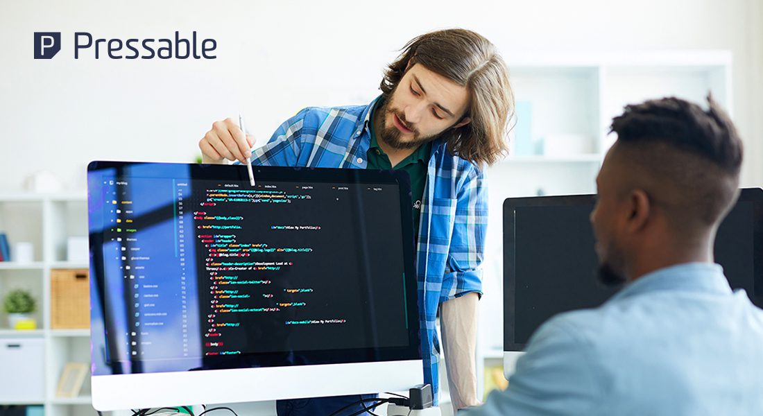 Two people collaborate on coding at a computer, surrounded by a modern office setting.