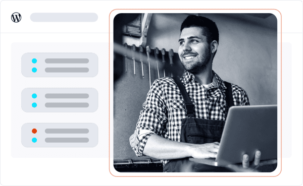 A person in overalls smiling, using a laptop in a workshop environment.