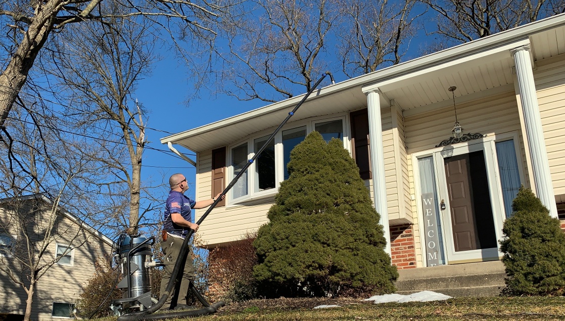 Technician pressure washing the upper siding of a house with a long wand