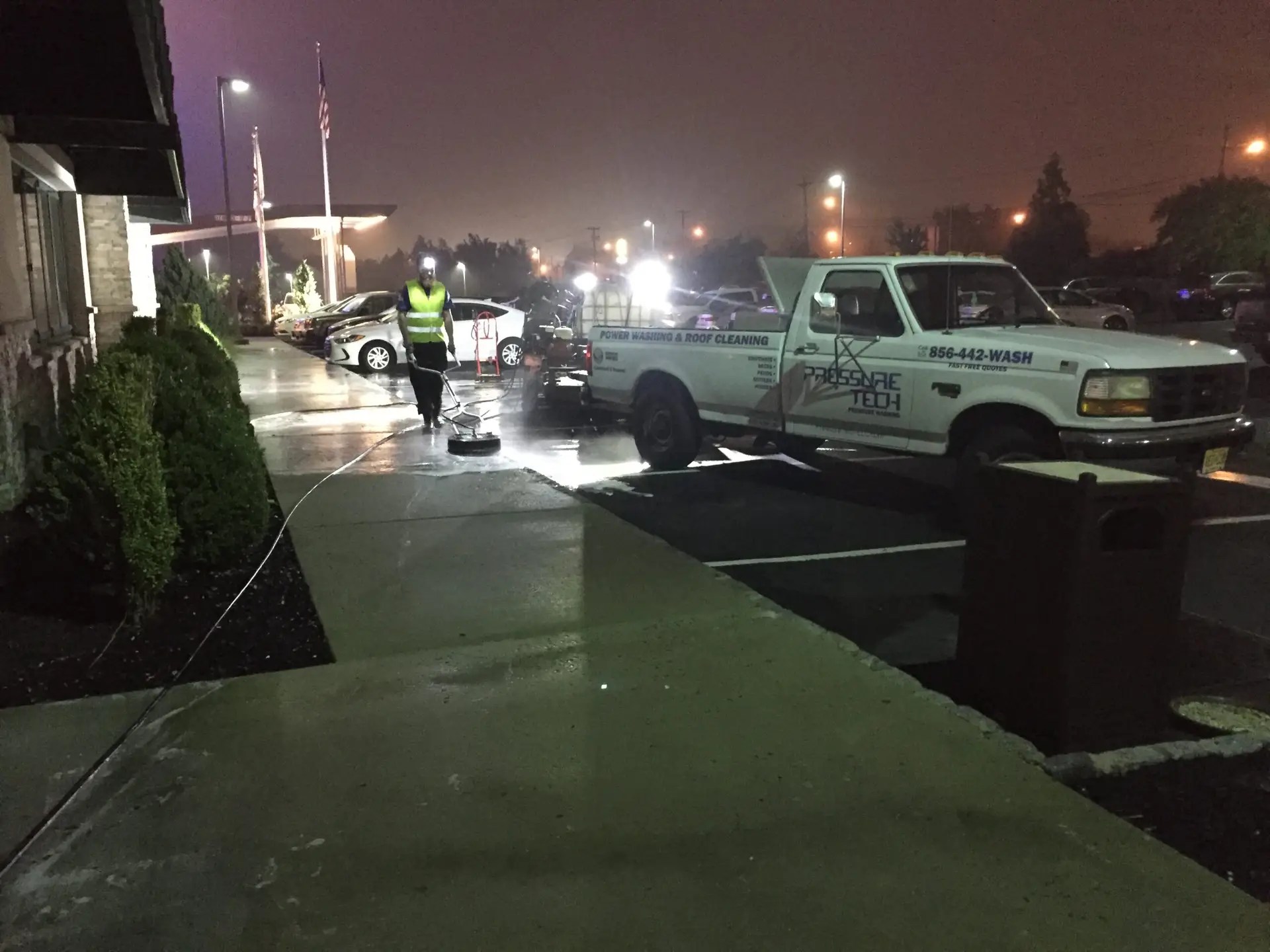 Pressure Tech truck and technician cleaning outside a commercial building at night