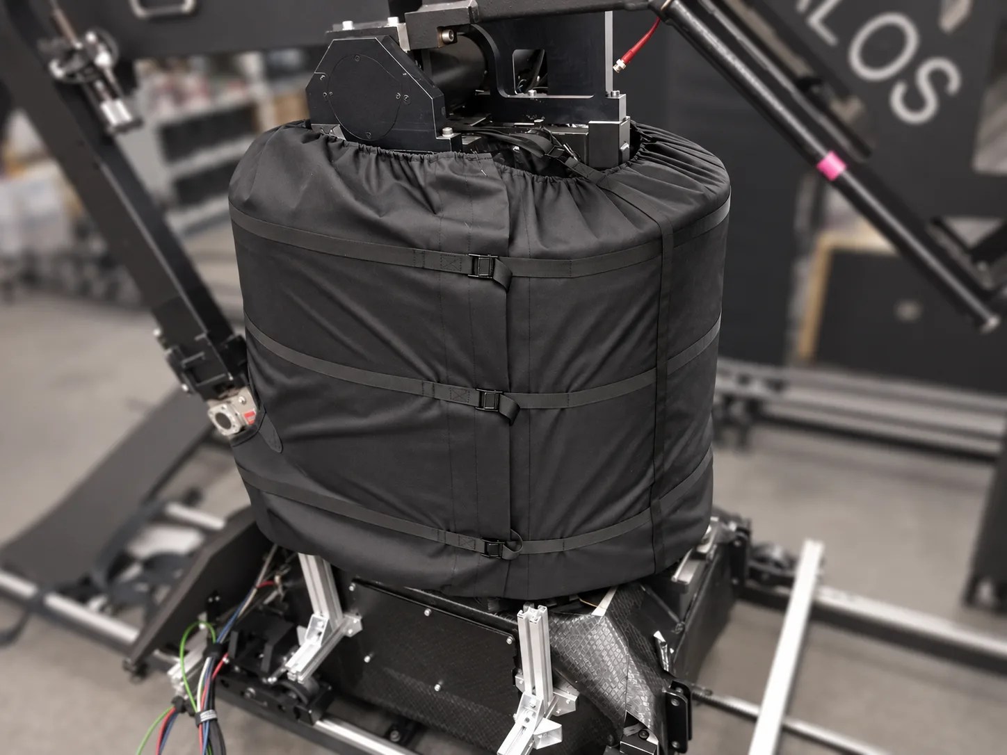 Fitted black Talos cover with retaining straps against a softly blurred workshop background