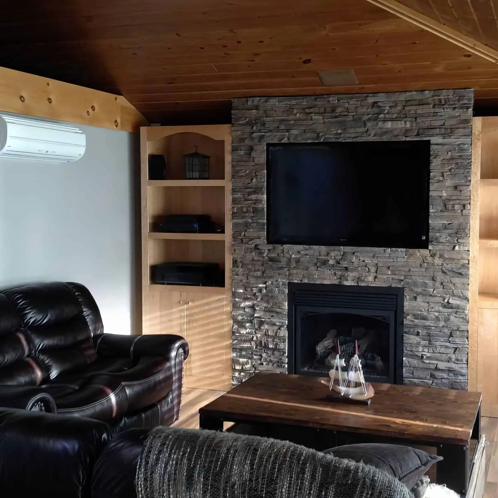 Conjunto de sala de estar con chimenea y televisión en pared de piedra.