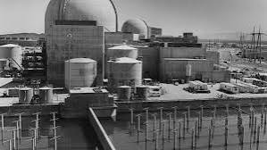 Black and white photo of a nuclear power plant, showing cooling structures and switchyard equipment.