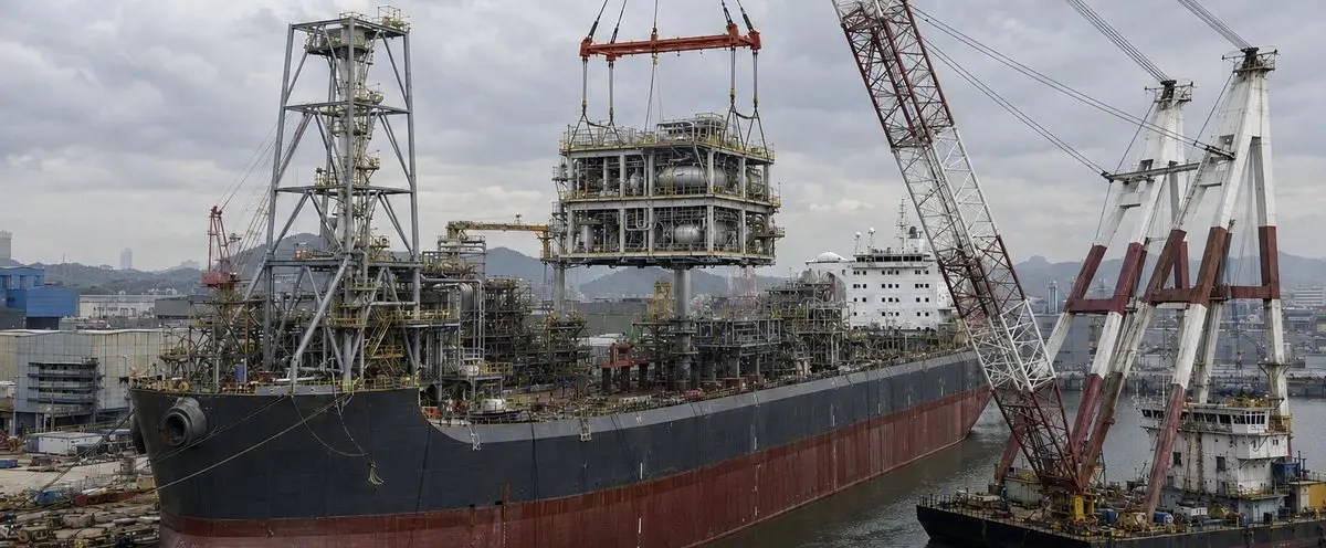 FPSO in a fabrication yard with a floating crane lifting a topsides process module aboard