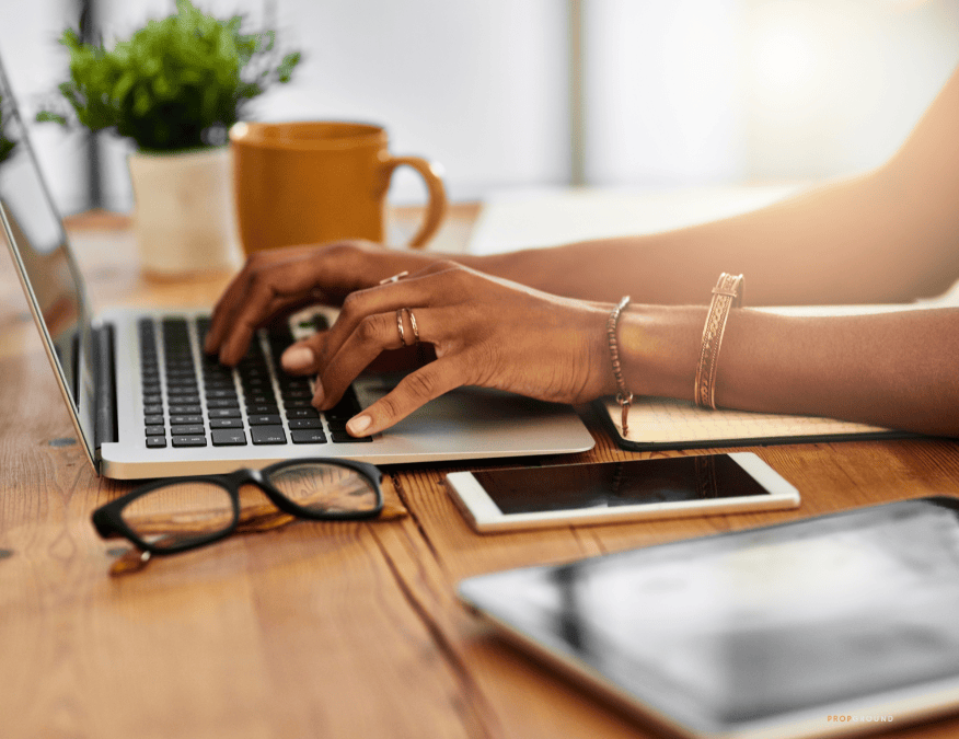 Real estate professional working on a laptop with a phone, tablet and notebook nearby