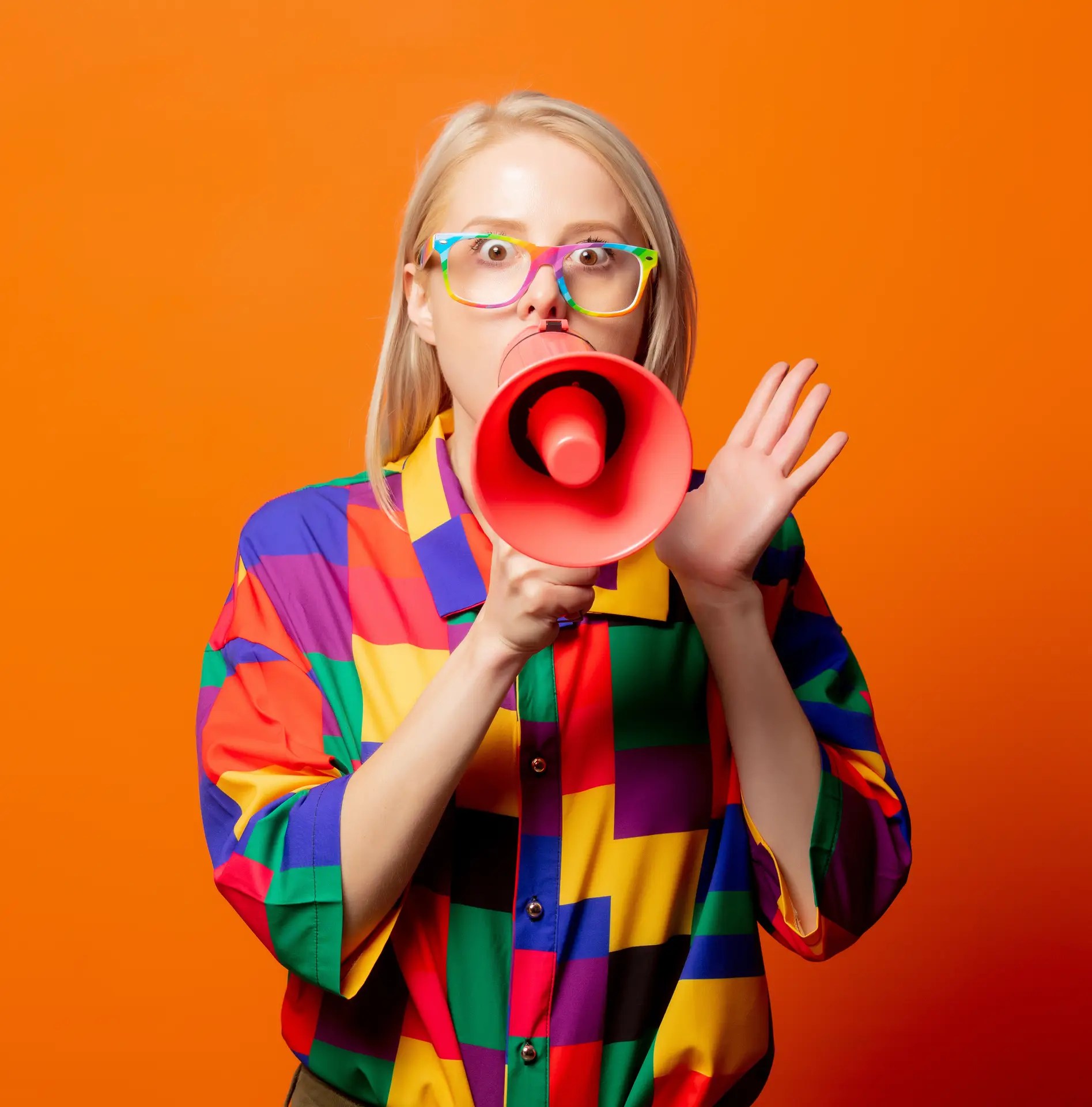 Style blonde in 90s clothes and rainbow glasses with megaphone on orange background
