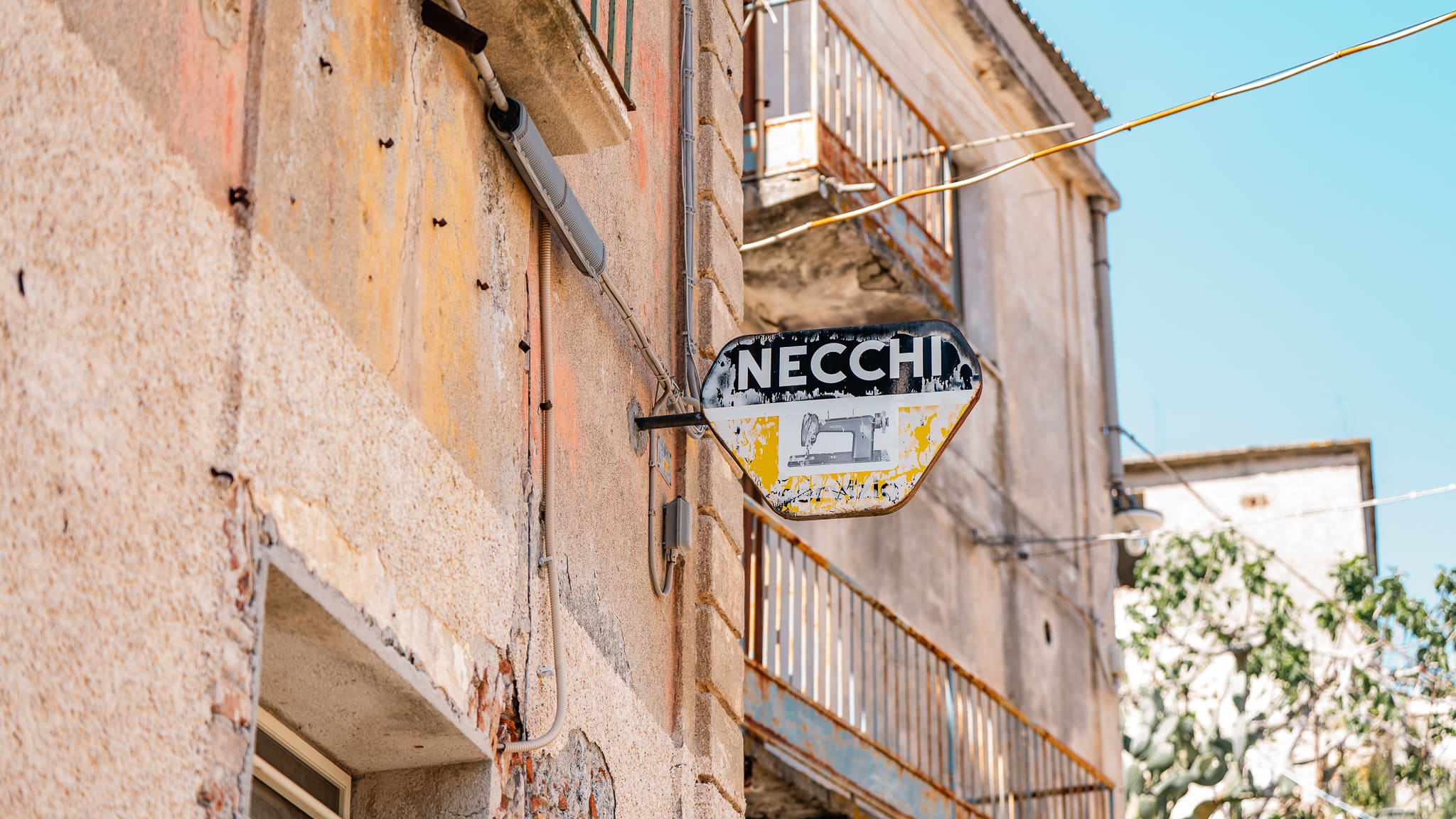 Vecchia insegna di un rivenditore di macchine da cucire su una facciata scrostata a Canolo Vecchia, borgo abbandonato dell'Aspromonte reggino.