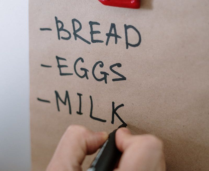 Gros plan d'une main écrivant une liste de courses avec un marqueur sur du papier brun.