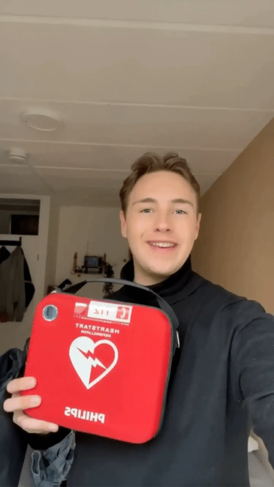 Young man holding red AED and smiling at the camera indoors.