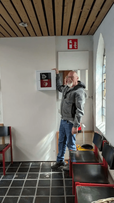 Man pointing at a red AED mounted beside a window.