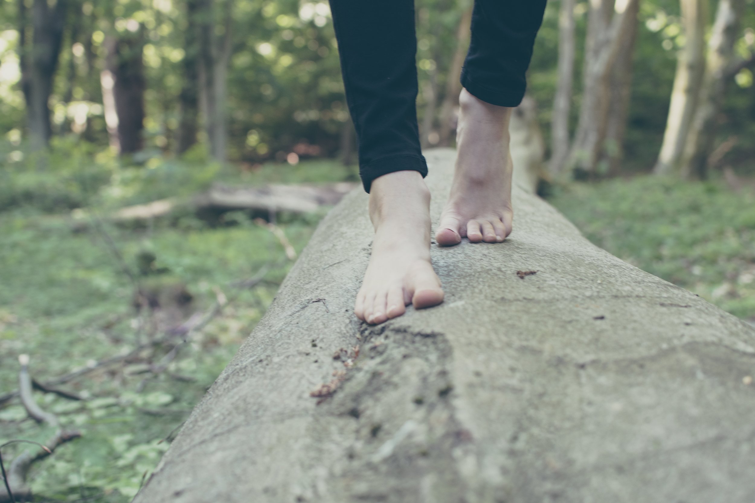 Person legs and feet walking across log barefoot in nature scene.