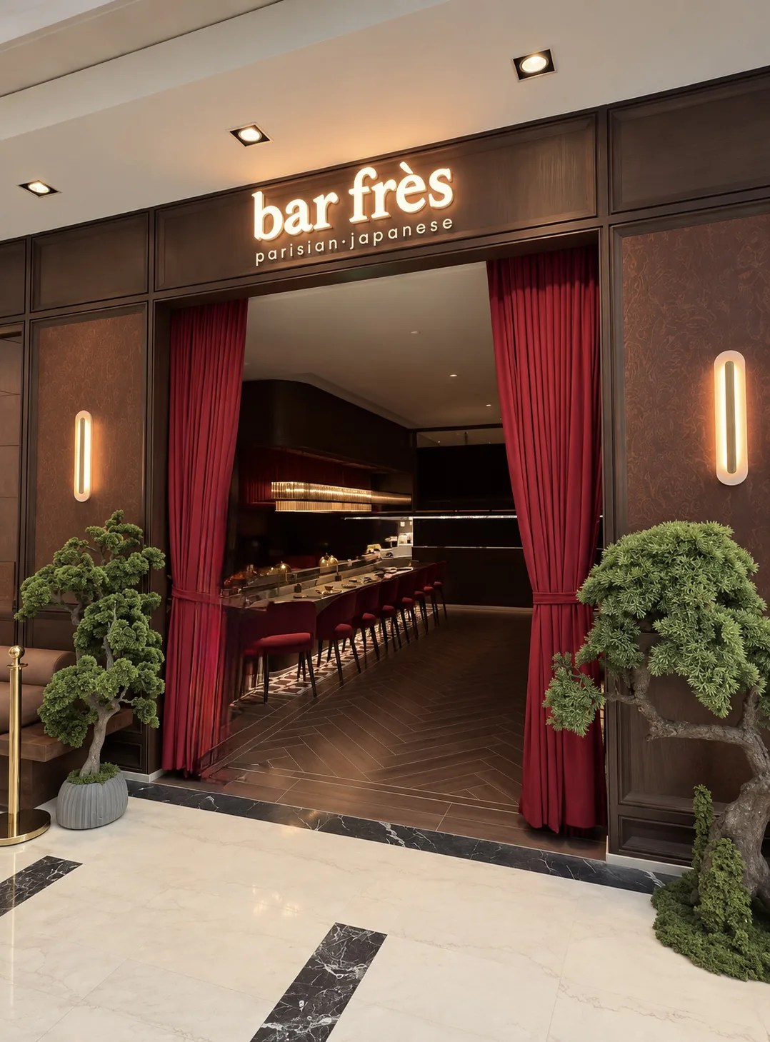 مدخل بار فريس في مجمع الراية، تعلوه لافتة bar frès parisian-japanese المضيئة، مع ستائر مخملية حمراء وشجرة بونساي على كل جانب.