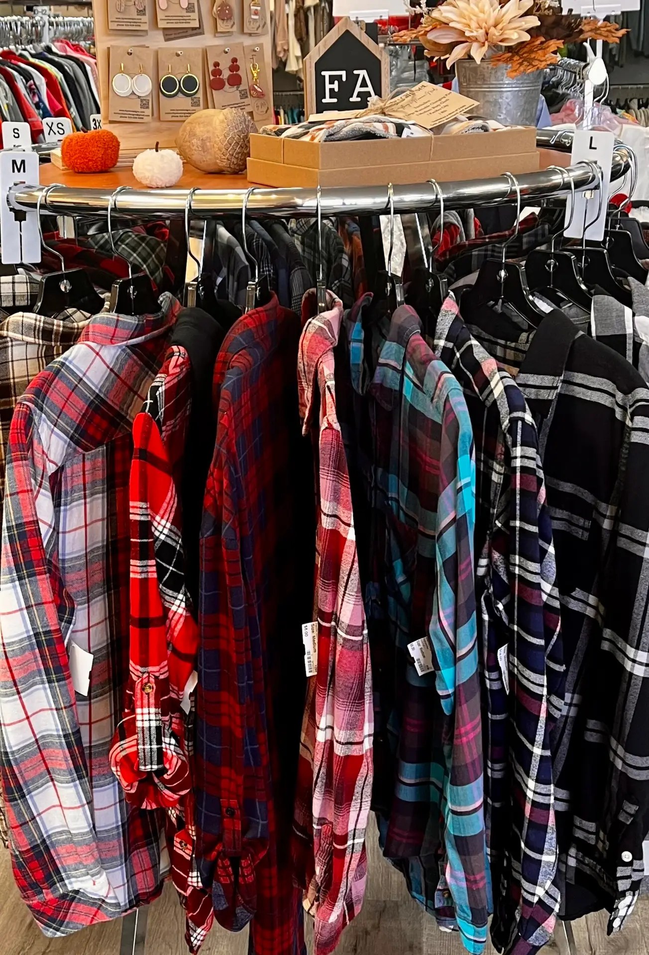 Flannel shirts on a round rack with fall decor at Quality Shoppe