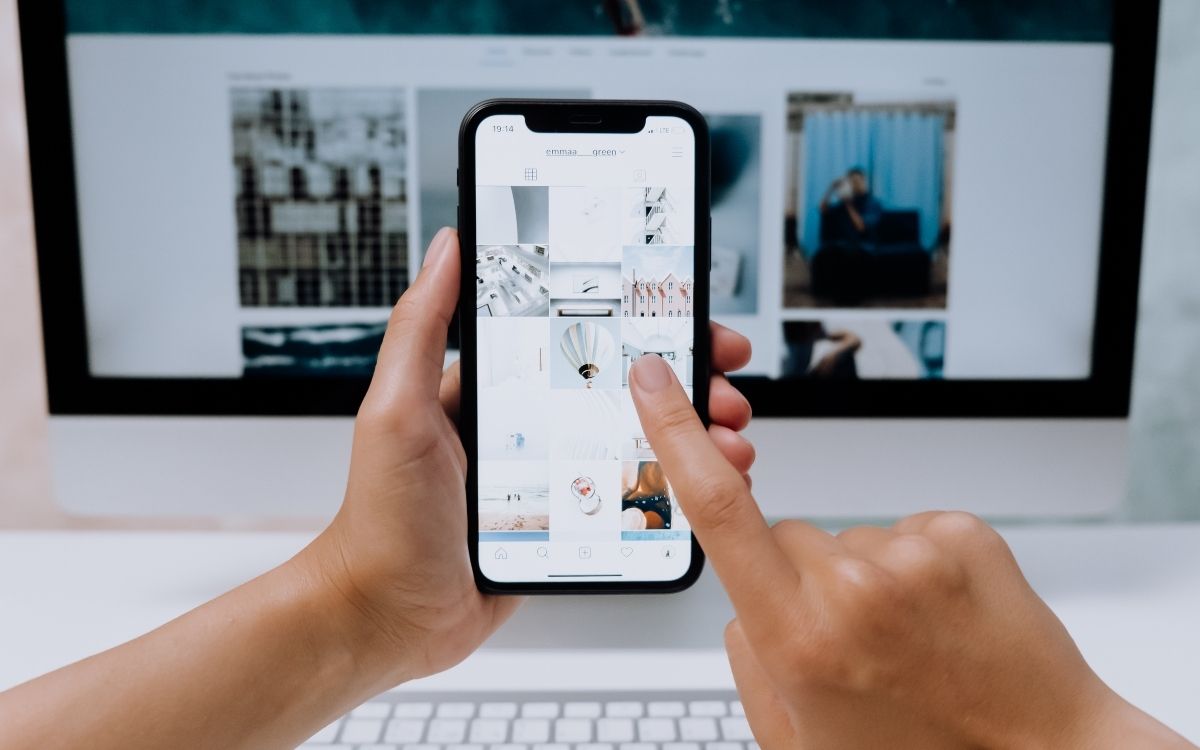 Person holding a phone pointing to an Instagram profile with various content.