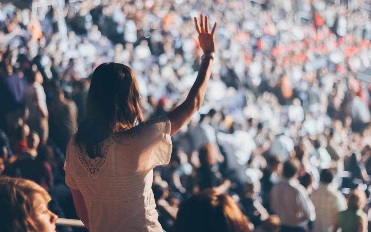 Woman in large crowd or audience raising an arm in excitement.