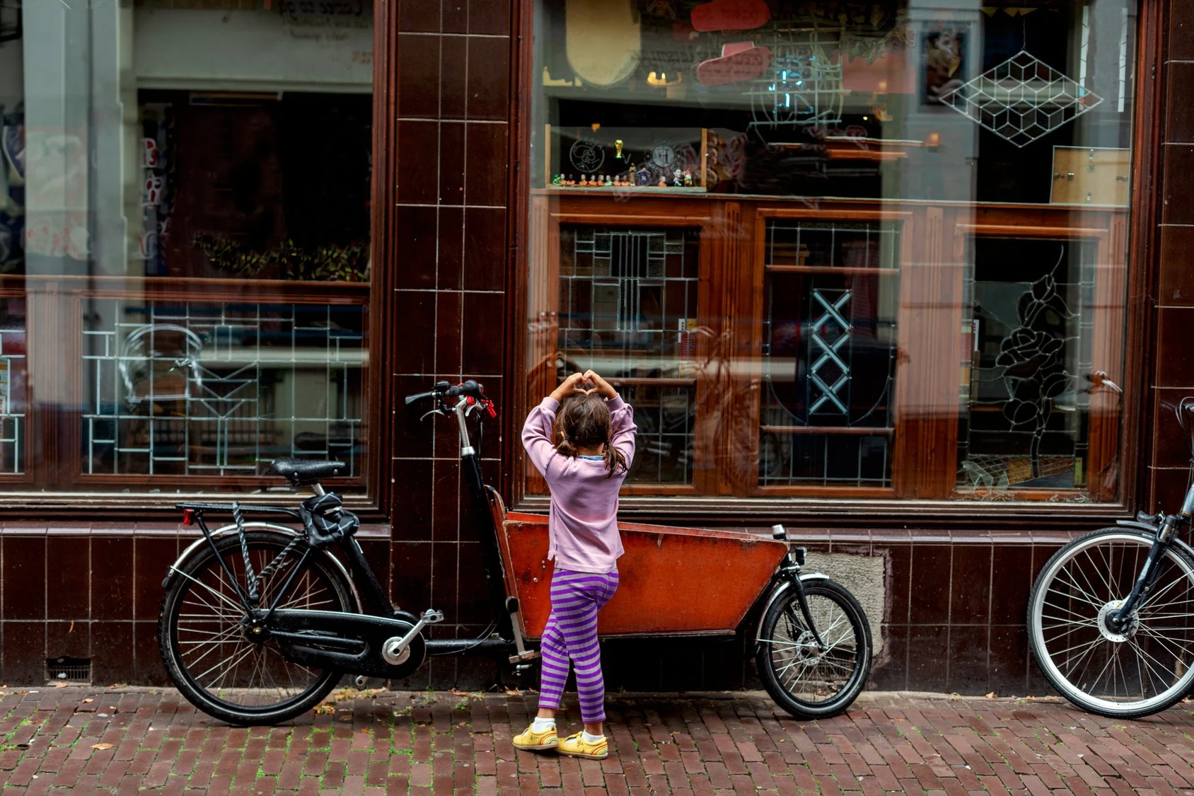 Lastenrad mit Sitzbank für Kinder vor einem Geschäft in Hamburg, daneben ein Kind auf dem Gehweg.