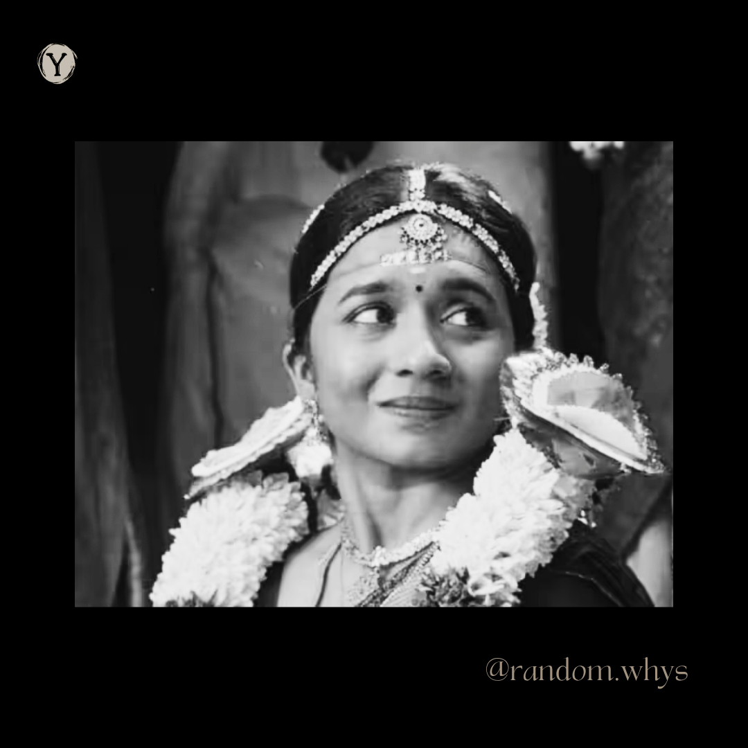 Black and white still of a young woman in bridal attire — a jewelled headpiece, matching earrings and necklaces, and thick white flower garlands over both shoulders. She looks off to her right with a small, restrained smile.