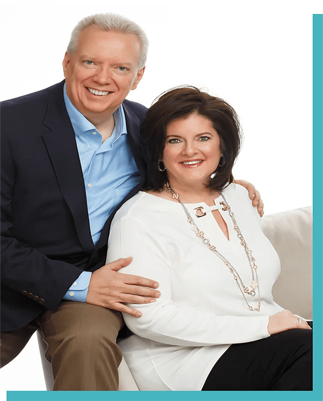 A smiling couple sits together, dressed in business attire.