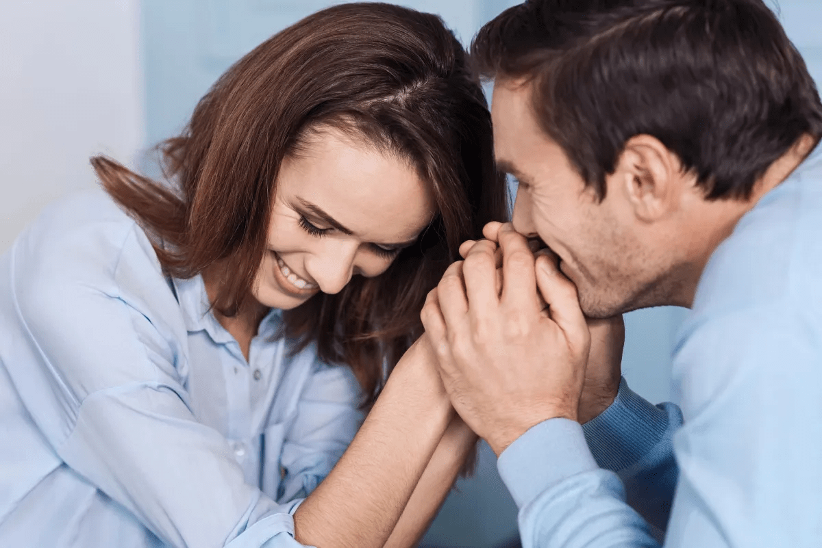 A couple is sitting closely, smiling and holding hands, suggesting affection.